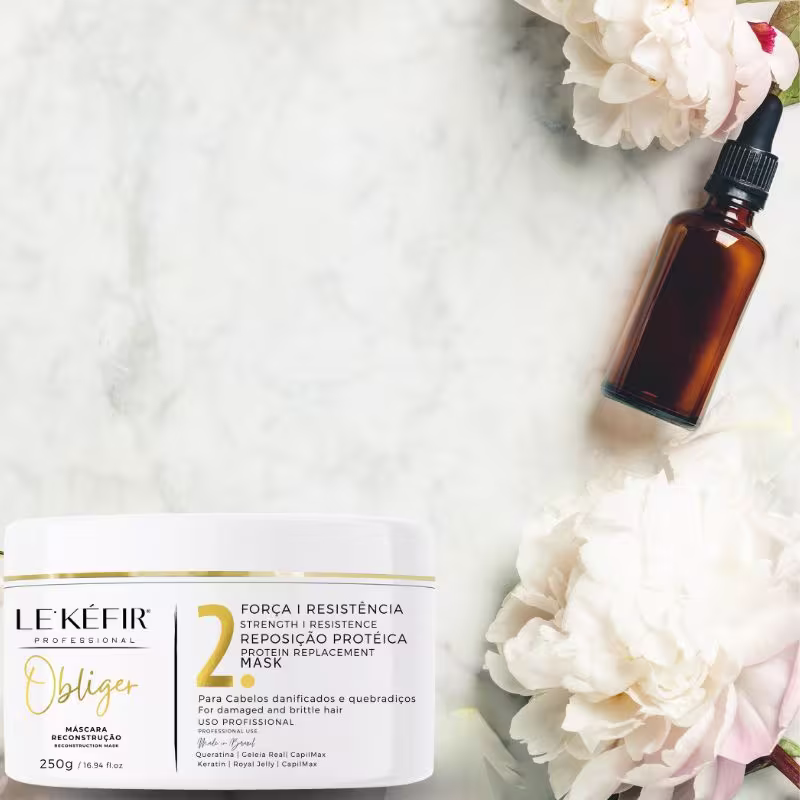 A imagem mostra um frasco âmbar contendo provavelmente um óleo ou sérum capilar. Ao lado, há uma embalagem da máscara capilar adornada com flores brancas, provavelmente hortênsias, criando um visual elegante e natural.