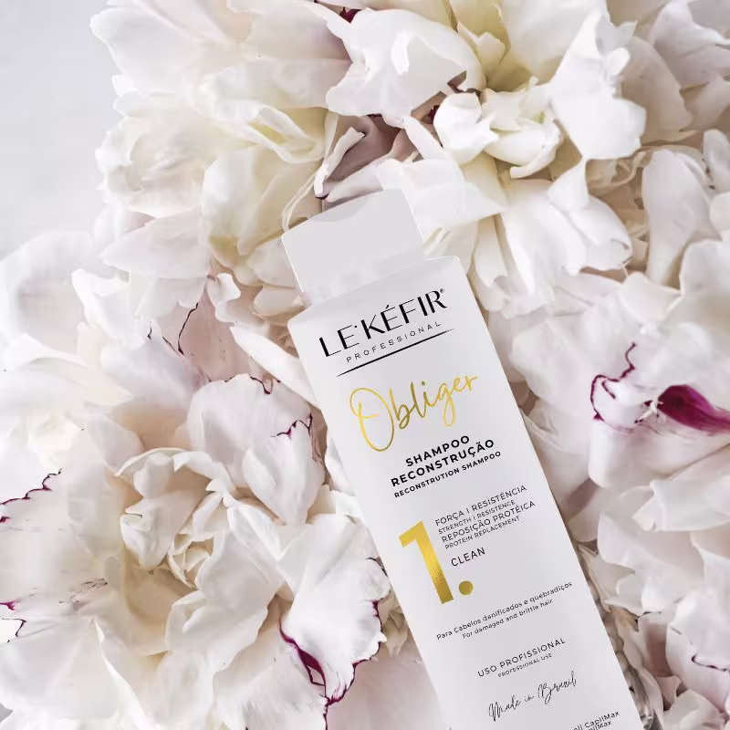 A imagem mostra o frasco do produto em destaque, rodeado por pétalas brancas de uma flor desmembrada. As pétalas têm algumas manchas avermelhadas. O cenário cria uma ambiente leve e delicado.