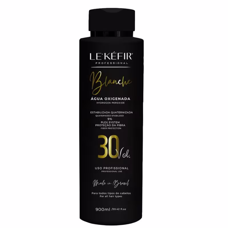 A imagem mostra a embalagem preta da água oxigenada posicionada sobre uma pedra clara, em um fundo bege, com folhas verdes decorando a cena, transmitindo uma atmosfera natural para esse cosmético capilar.