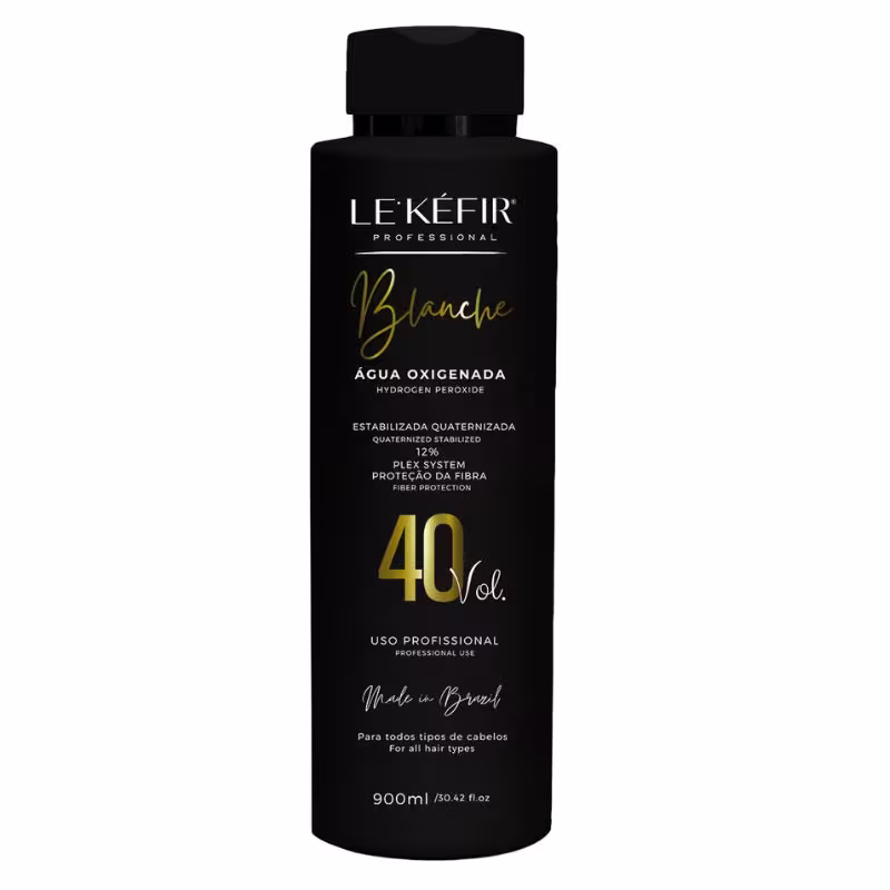 A imagem mostra a embalagem preta da água oxigenada posicionada sobre uma pedra clara, em um fundo bege, com folhas verdes decorando a cena, transmitindo uma atmosfera natural para esse cosmético capilar.