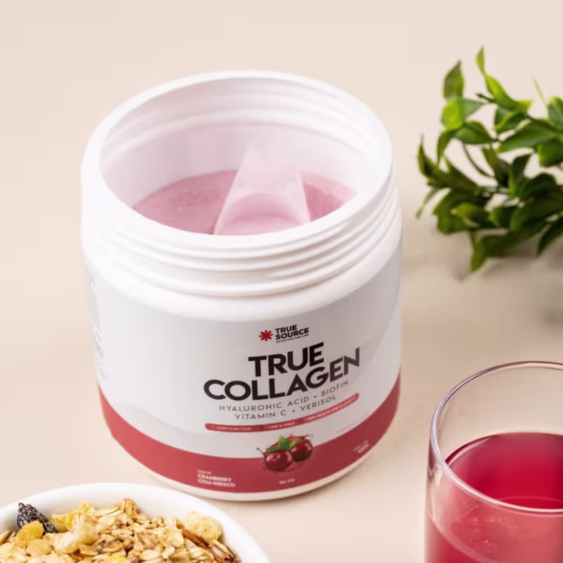 Produto de beleza da marca True Source, um suplemento de colágeno em pó.  Rótulo vermelho com o nome "True Collagen". Ao lado, um copo transparente com um líquido rosa, indicando o suplemento dissolvido em água.