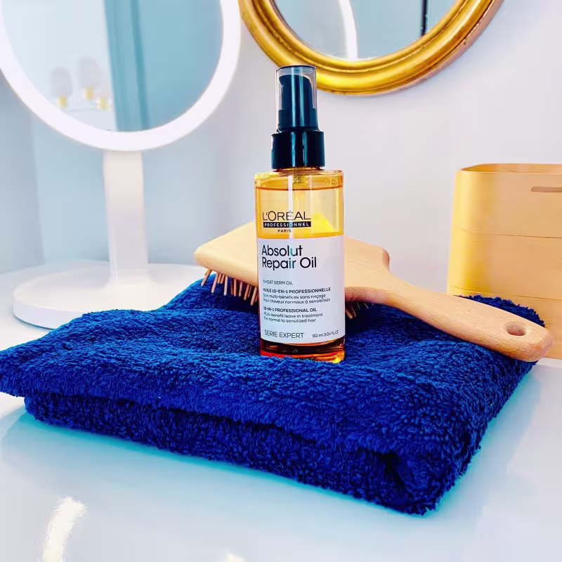 O produto apresentado é um óleo de reparação capilar da linha Serie Expert da L'Oreal Professionnel. A embalagem é um frasco plástico transparente âmbar com tampa preta. O rótulo indica que se trata do "Absolut Repair Oil".