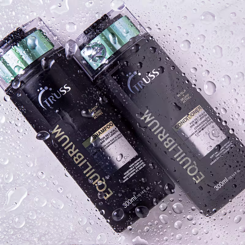 A imagem apresenta um shampoo e um condicionador, todos com embalagens plásticas pretas de 300ml. Os frascos tem o nome da linha "Equilibrium" e o logo da Truss.