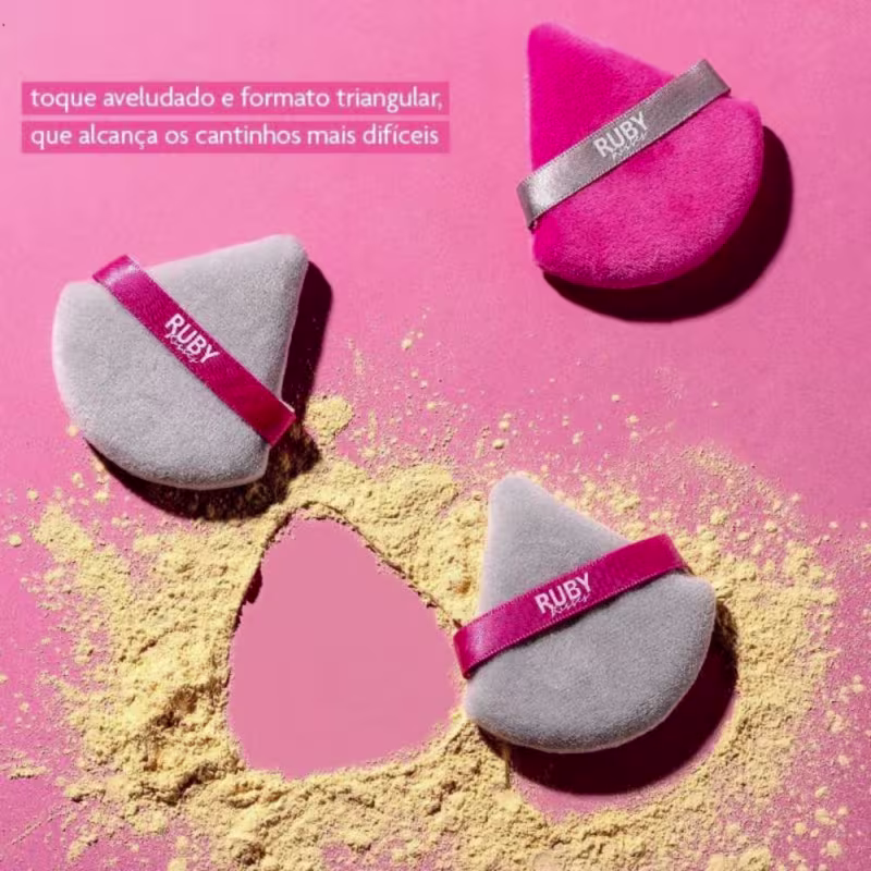 A imagem mostra três esponjas em meio à pó de maquiagem, num fundo rosa e a informação de toque aveludado, formato triangular para alcançar os cantinhos mais difíceis.