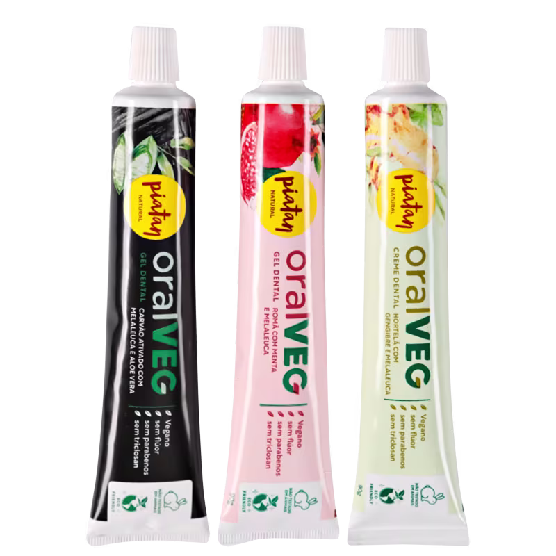 Três tubos de creme dental vegano da marca Piatan. Os tubos têm embalagens plásticas cilíndricas com tampas brancas rosqueáveis. As cores dos tubos são preto, vermelho e branco, respectivamente.