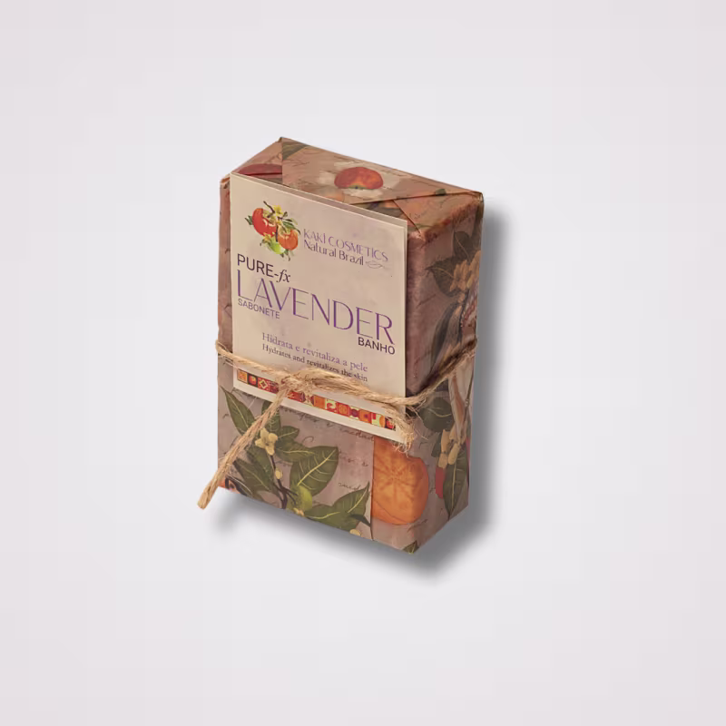 Caixa retangular de papelão com estampa de folhas e frutas alaranjadas. Rótulo com o texto "Pure & Lavender Banho". Fita de papel amarrada ao redor da caixa. Cores predominantes são marrom, laranja e verde. Embalagem com design rústico e natural.