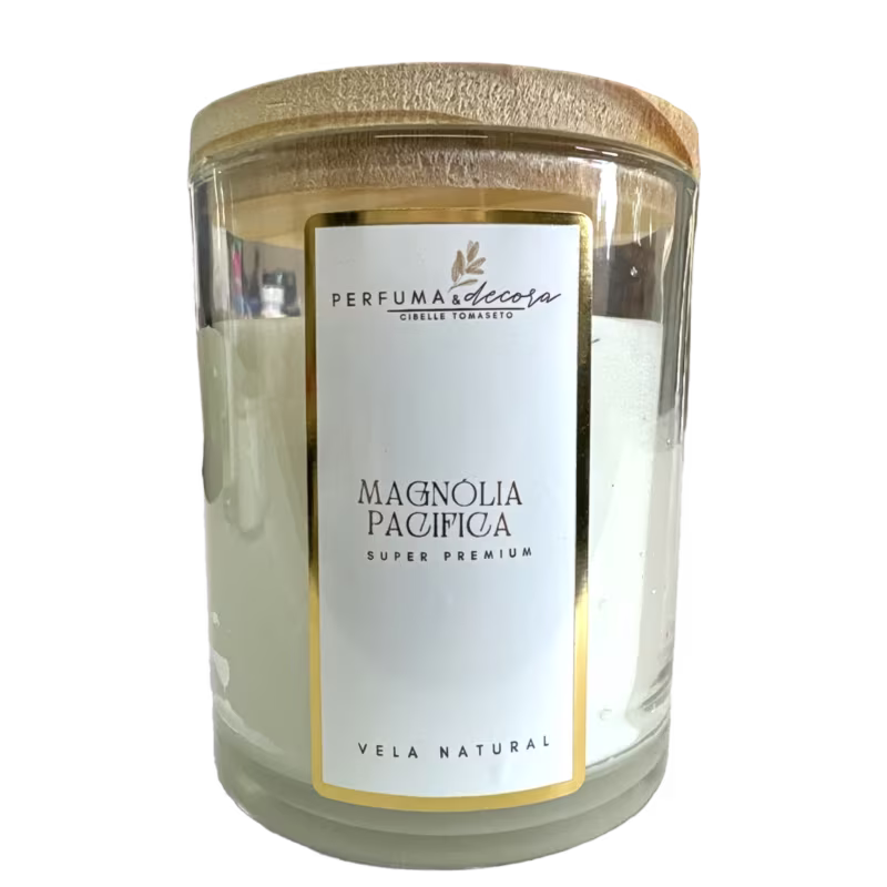 Vela natural em frasco de vidro transparente com tampa dourada. A embalagem tem um rótulo branco com o nome "Magnolia Pacifica Super Premium" em letras pretas e o logotipo "Perfuma & Decora" em dourado.