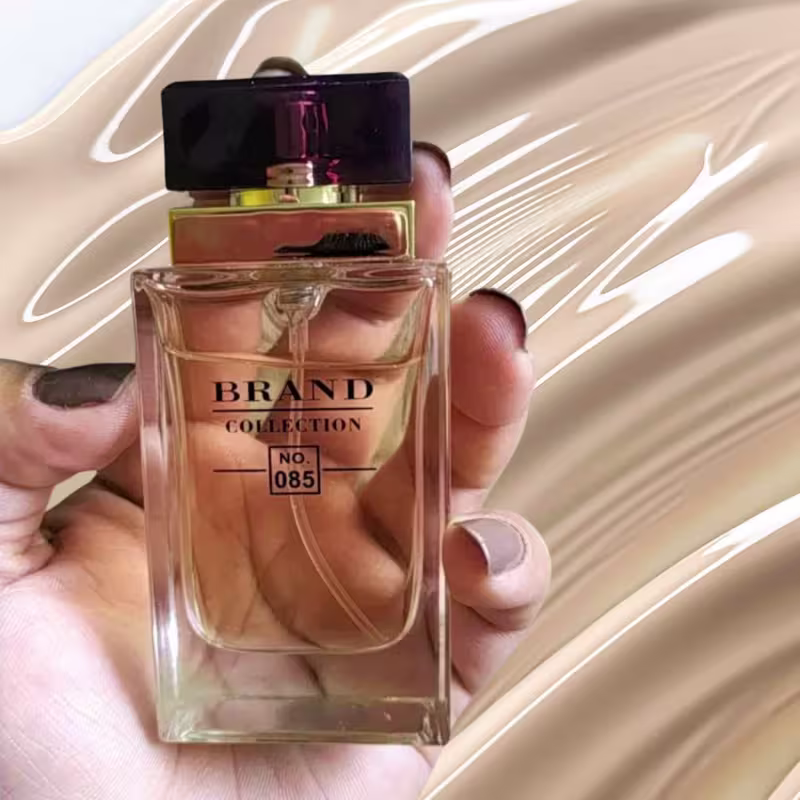 A imagem mostra uma mão branca feminina segurando um frasco de perfume em um fundo bege de textura cremosa.