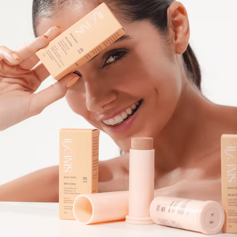 A imagem mostra uma modelo segurando a caixinha do produto próximo ao rosto dela, além de caixinhas e produtos numa bancada.