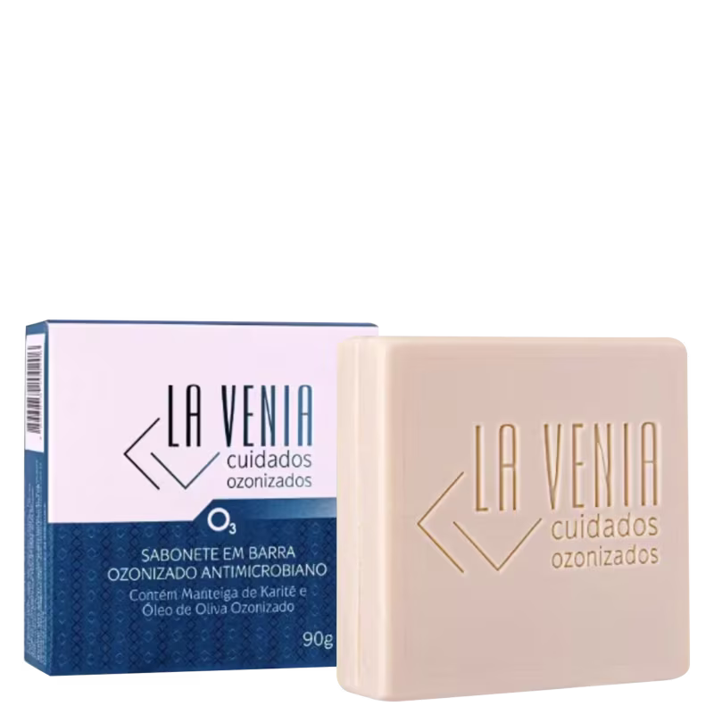 A imagem mostra um sabonete em barra antimicrobiano ozonizado da marca La Venia Cuidados Ozonizados. O produto vem em uma embalagem retangular de papelão nas cores branca e azul marinho. Enquanto a barra do sabonete tem cor bege.