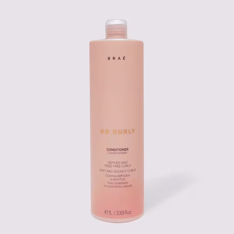 Frasco de condicionador Brae Go Curly, com embalagem rosa clara e rótulo com texto em amarelo e branco, indicando que o produto é para cachos definidos e sem frizz.