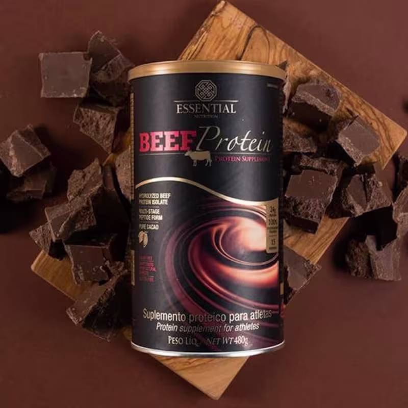 A imagem mostra uma lata de suplemento com fundo preto em meio a pedaços de chocolate.