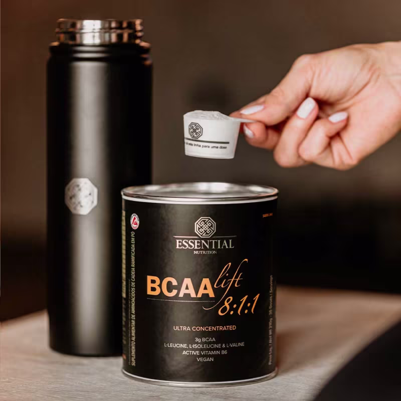 A imagem mostra a lata aberta e uma mão segurando a colher medidora com o produto dentro.