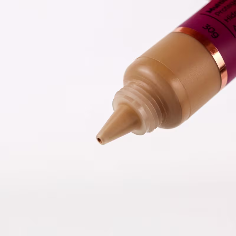 Base em tubo cilíndrico de plástico. A ponta do tubo mostra a cor bege médio da base. O tubo tem uma faixa dourada próxima à ponta.