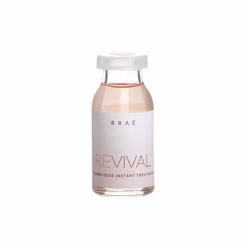 Produto de tratamento capilar instantâneo da linha Revival da marca Braé. Frasco de vidro transparente contendo um líquido de cor rosada. Rótulo branco com o nome da marca "Braé" e o nome do produto "Revival Power Dose Instant Treatment" em letras pretas.