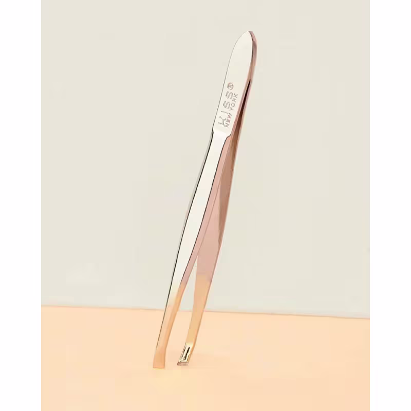 A imagem mostra a pinça de sobrancelha em metal com cabo longo e curvado. A pinça é de cor prateada com detalhes em dourado metálico.