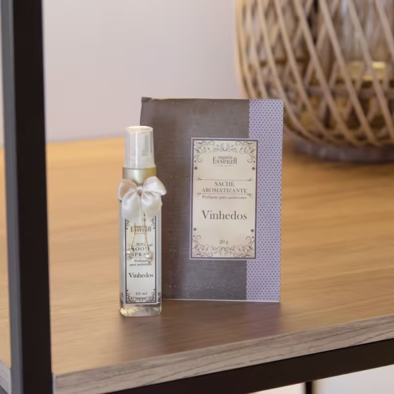 Embalagem com rótulo cinza e branco, contendo a marca "Empório Essenza" e o nome do produto "Vinhedos". Caixa cinza com detalhes em poá acompanha o frasco.