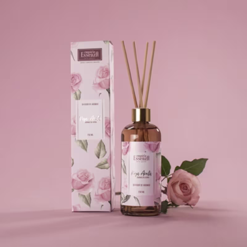 Frasco de difusor de aromas da marca Empório Essenza Serra Gaúcha, com rótulo rosa e branco exibindo flores, contendo líquido âmbar e hastes de madeira, em embalagem decorativa com ilustrações florais.