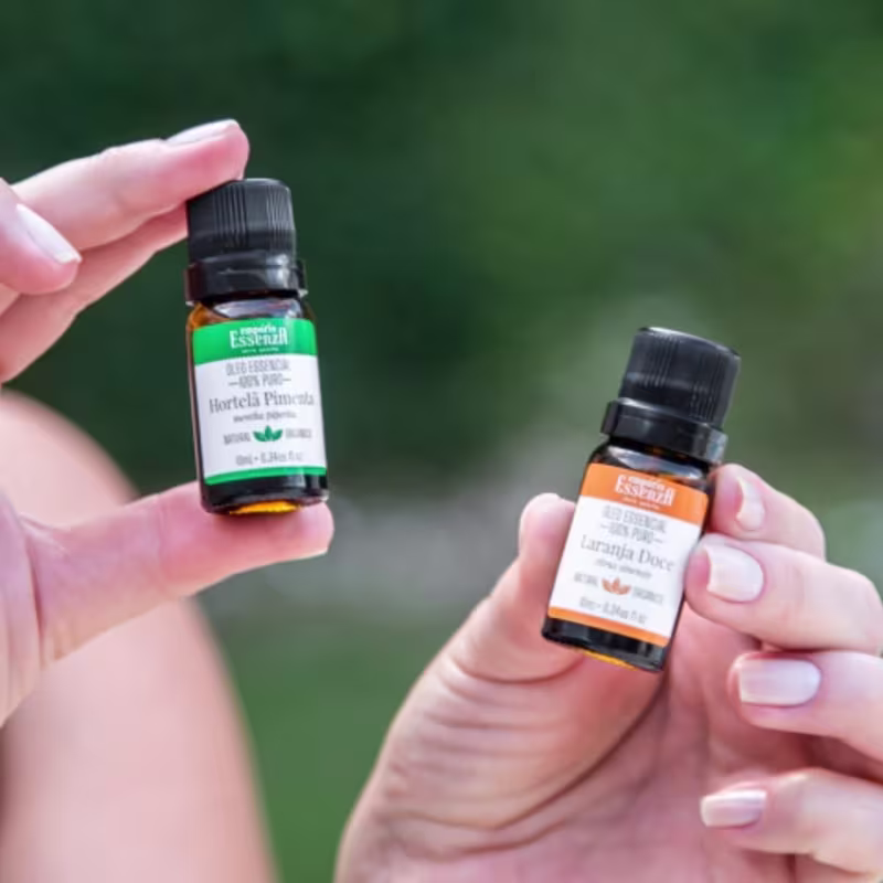 Dois frascos de óleos essenciais da marca Empório Essenza Serra Gaúcha, um com rótulo verde contendo Hortela Pimenta e outro com rótulo laranja contendo Laranja Doce, ambos em embalagens de vidro com tampas pretas.
