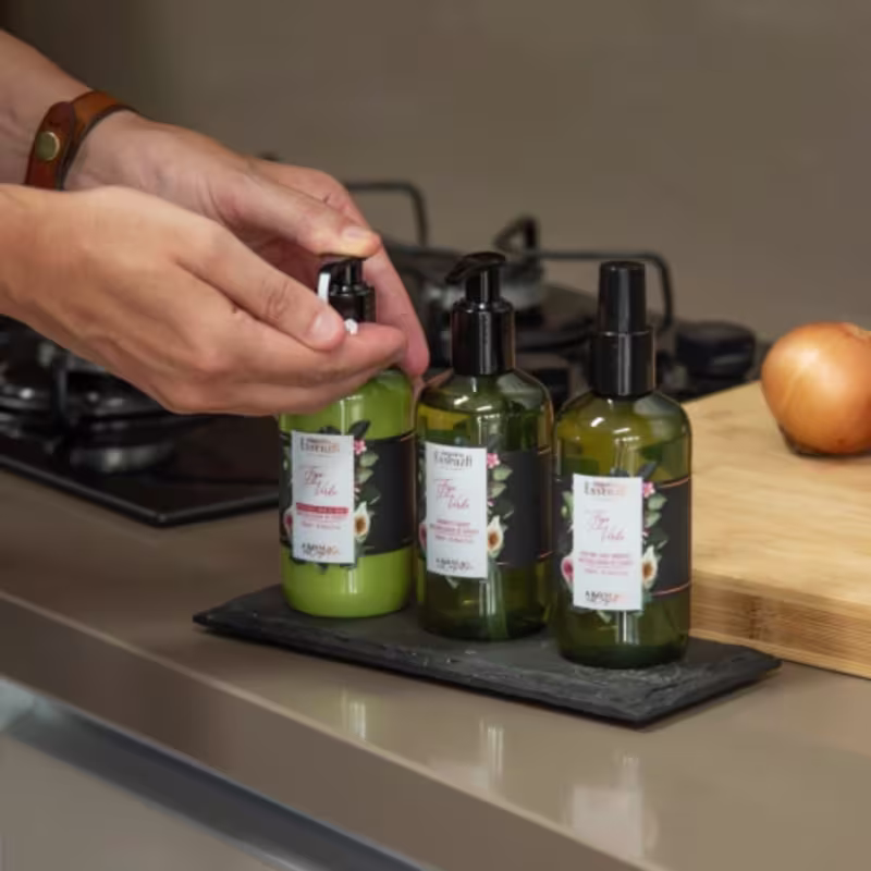 Frascos de produtos de beleza da marca Empório Essenza Serra Gaúcha, com rótulos verdes e detalhes em preto, dispostos sobre uma superfície de madeira.
