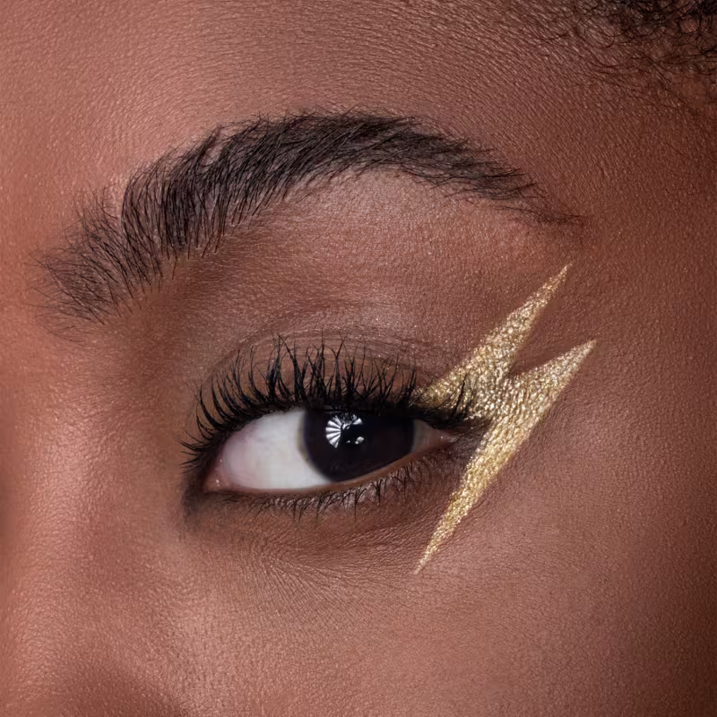 Sombra dourada metálica aplicada em formato de raio, evocando o icônico símbolo na testa do protagonista. Delineador preto intenso realçando os olhos. Cílios longos e volumosos com rímel escuro. Sobrancelha escura bem delineada.