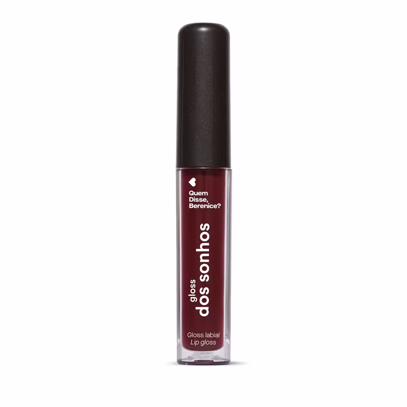A imagem mostra um gloss labial em uma embalagem cilíndrica com a tampa preta e o tubo transparente permite ver o tom roxo brilhante do gloss e a marca Quem disse, Berenice? e a linha estampados no frasco.