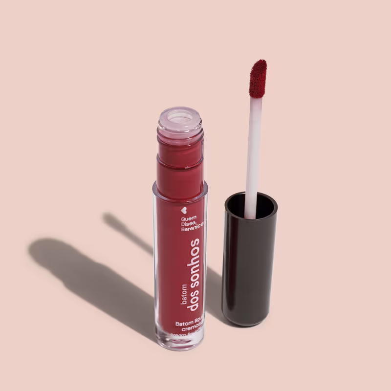 A imagem mostra o frasco do batom labial e ao lado há um aplicador de espuma na cor branca com a ponta no tom marrom e base preta.