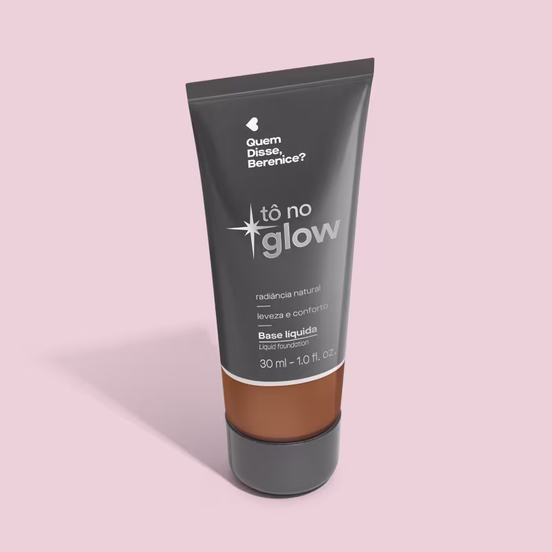 Base líquida em bisnaga preta com base transparente onde é possível ver o tom do produto. Fundo rosa.