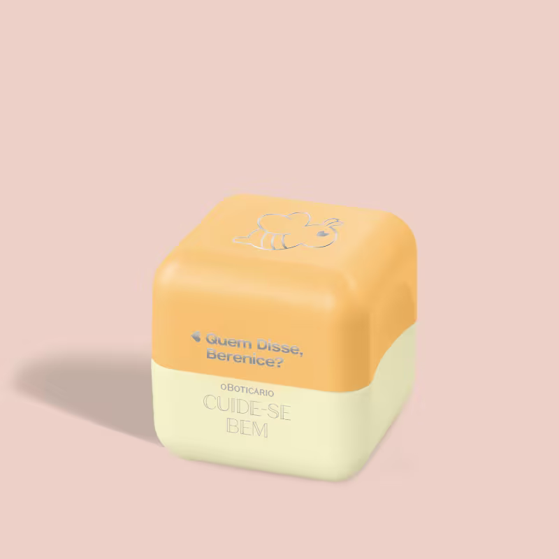Balm Labial em formato hexagonal, com duas seções de cores distintas de amarelo. A parte superior é amarela com um desenho estilizado de uma abelha. Há um texto em português que diz "Quem disse, Berenice?" e "Oboticario CUIDE-SE BEM".