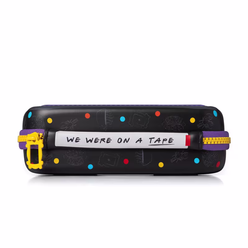 Bolsa preta com estampas coloridas de câmeras, fitas e outros símbolos. Texto "We were on a tape" escrito na parte frontal. Objeto de uso pessoal ou de viagem com design divertido e informal.