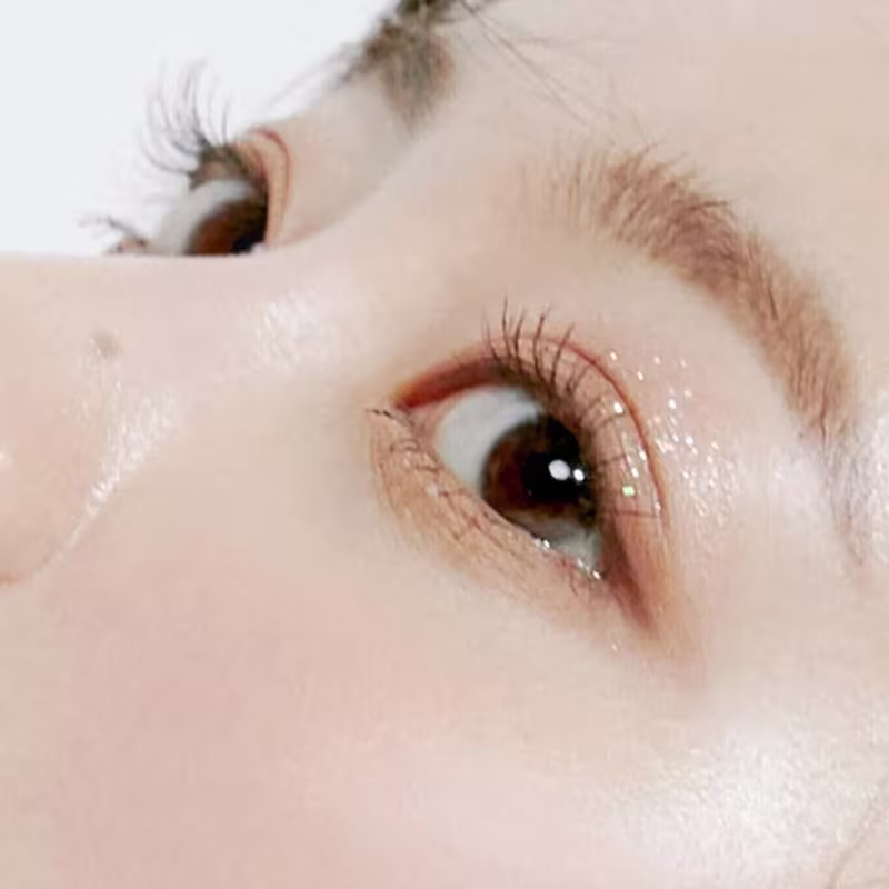 A imagem mostra um close-up de um olho humano com cílios longos e escuros, sugerindo um produto de beleza da marca rom&nd, possivelmente um rímel ou delineador, em um ambiente iluminado e com fundo claro.