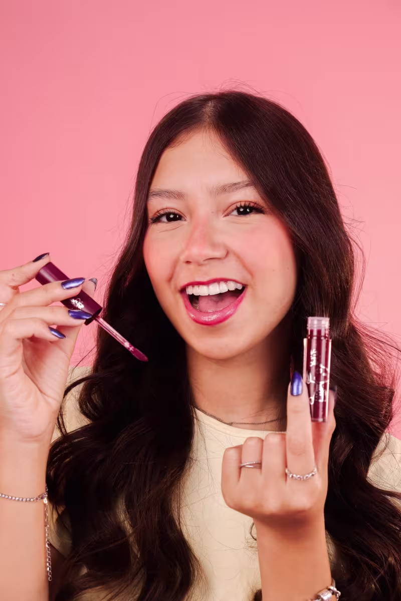 Modelo sorridente segura o gloss labial. Ela parece estar aplicando ou exibindo os produtos.