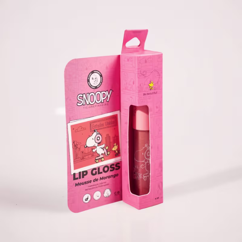 A embalagem é uma caixa rosa com ilustrações do personagem Snoopy e informações sobre o produto A caixa possui um design simples e minimalista, com o logotipo da marca e a indicação de que o produto é um lip gloss.