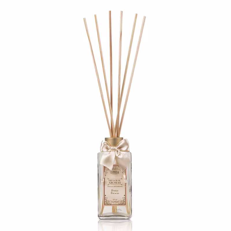 Difusor de aromas em frasco de vidro transparente com tampa dourada e laço de cetim bege. Rótulo com texto "Difusor de Aromas" e "Frutas Frescas". Hastes de madeira inseridas no frasco para dispersão do aroma.