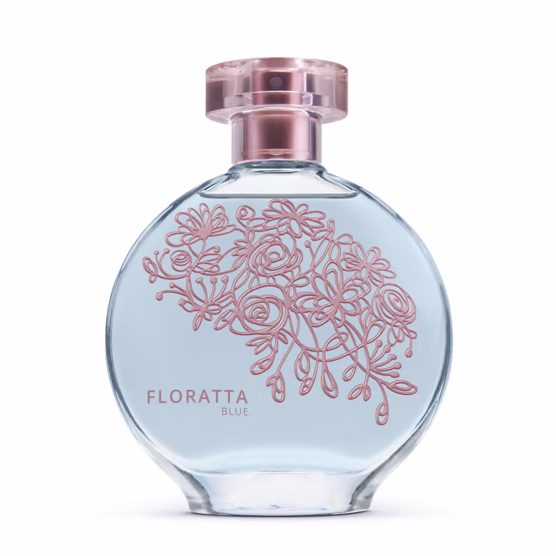 A imagem mostra um frasco de perfume da linha Floratta Blue. O frasco é de vidro transparente com um design arredondado. Há um padrão floral estilizado em tons de rosa desenhado sobre o fundo azul claro do frasco. A tampa é cor de rose gold metálico.