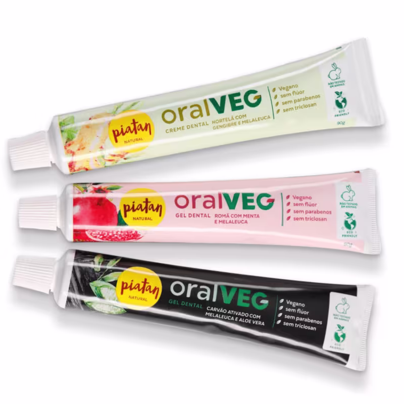 São três tubos de creme e gel dental veganos da marca Piatan Natural. O primeiro é branco, contendo hortelã e gengibre com melaleuca. O segundo é rosa com ilustração de romã, menta e melaleuca. O terceiro é preto com carvão ativado, melaleuca e aloé vera.