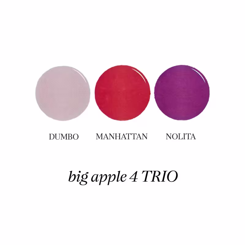 Três sombras de maquiagem em formato circular, nas cores cinza, vermelho e roxo, com os nomes "DUMBO", "MANHATTAN" e "NOLITA" impressos abaixo. Trata-se da coleção "big apple 4 TRIO" de produtos de beleza.