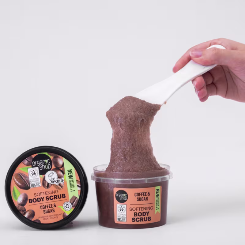 A imagem mostra a embalagem destampada e uma mão retirando um pouco do produto com a espátula.