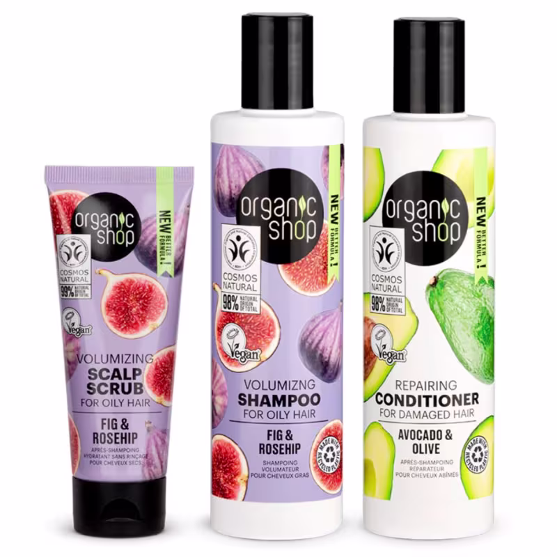 A imagem mostra um shampoo em frasco plástico branco com rótulo lilás e imagens de figo. Há um tubo lilás com o esfoliante capilar com o mesmo design do shampoo. Por fim, há um frasco branco com o condicionador e o rótulo com abacates espalhados.