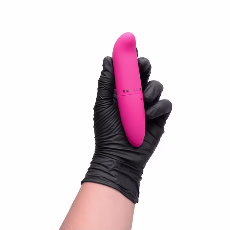 Vibrador rosa em formato alongado, com acabamento liso e brilhante, seguro por uma mão enluvada em tecido preto. O produto apresenta um painel de controle com botões e indicadores.