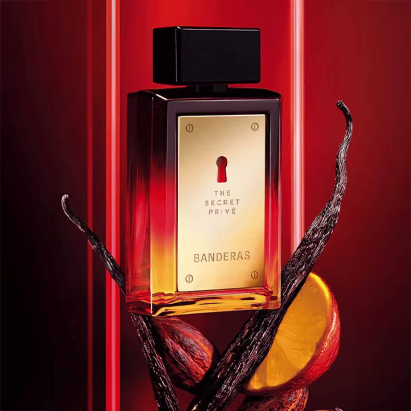 Frasco do perfume Secret Privé Banderas, com fundo de luzes neon e imagens de alguns ingredientes do perfume, como laranja, baunilha e cardamomo.