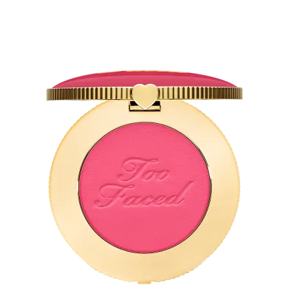 Blush compacto de maquiagem com embalagem redonda dourada. A tampa superior é rosa com a inscrição "Too Faced" em letras cursivas. Um pequeno coração dourado adorna o centro da tampa.