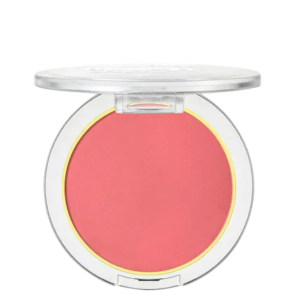 A imagem mostra um blush compacto de cor rosa em uma embalagem plástica transparente. O blush tem um acabamento fosco e está disposto em um estojo redondo. Em volta do pó compacto rosa, há um aro amarelo que realça a cor do produto.