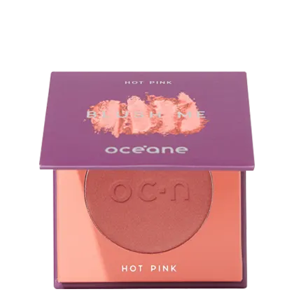 A imagem mostra o produto Blush Me da marca Océane. É uma embalagem quadrada de cor roxa que está semiaberta mostrando a cor do blush em um tom rosa com leve brilho perolado. A parte interna da embalagem é de cor pêssego claro,