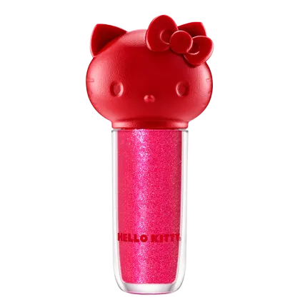 Maquiagem em formato cilíndrico com a cabeça da personagem Hello Kitty como tampa. A parte superior é vermelha com detalhes em relevo que representam os olhos, orelhas e laço da Hello Kitty. É possível ver a cor do produto pelo corpo transparente.