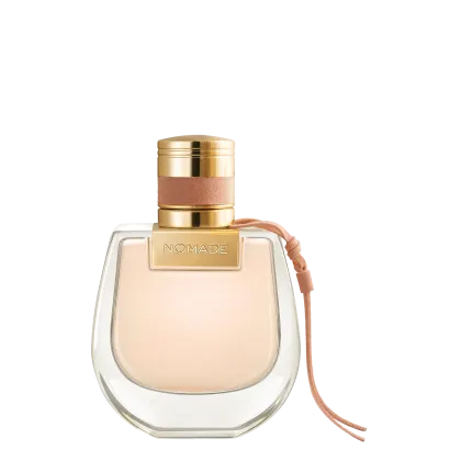 Perfume em frasco de vidro transparente com formato arredondado. A tampa é dourada com detalhes em couro rosé. O nome "NOMADE" está gravado em letras douradas na parte superior da tampa. O líquido dentro do frasco é de uma tonalidade bege claro.