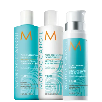 Produtos para cabelos cacheados da linha Moroccanoil Curl. Três embalagens plásticas cilíndricas: um shampoo de 250ml, um condicionadorde 250ml e um creme modelador de cachos de 250ml. As cores predominantes são azul claro, branco e laranja.