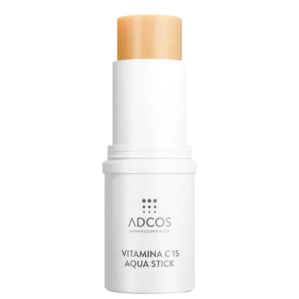 Produto em formato stick, com embalagem cilíndrica branca. O rótulo na embalagem branca exibe o logotipo da marca Adcos e o nome do produto "Vitamina C 15 Aqua Stick". Na parte superior aparece um pedaço do produto em cor amarelo alaranjado.
