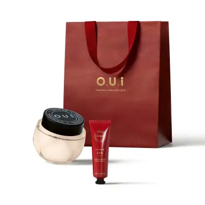 Conjunto de produtos de beleza da marca O.U.i., incluindo um frasco de creme e um tubo de creme para as mãos, embalados em uma sacola vermelha com o logotipo da marca.