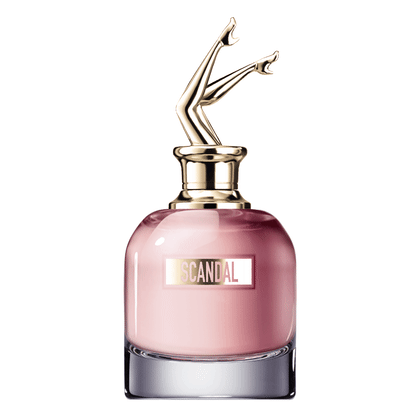 Perfume em frasco de vidro rosa com tampa metálica dourada em forma de pernas femininas. O frasco tem base cromada e o rótulo exibe o texto "SCANDAL" em letras maiúsculas douradas.